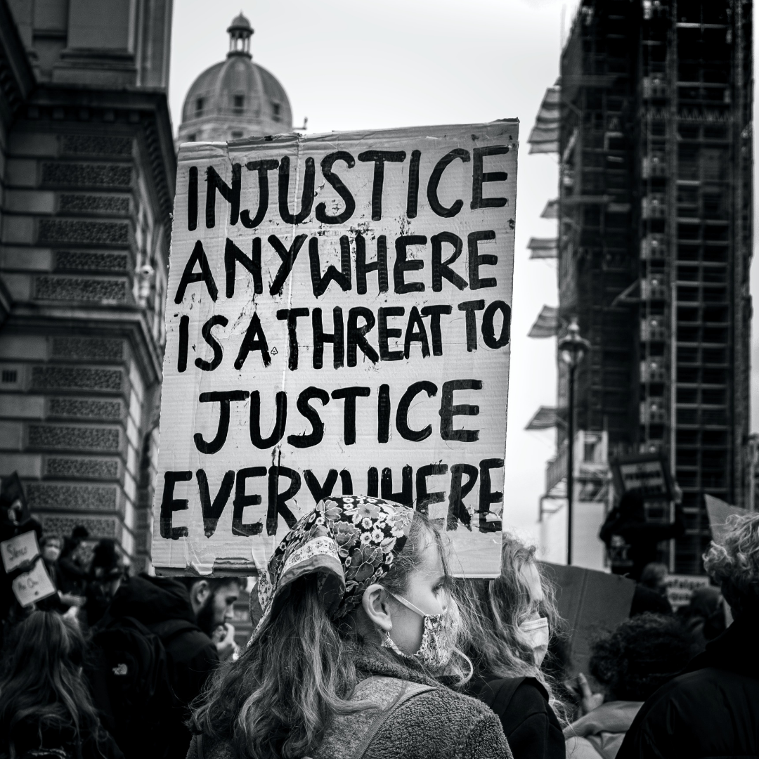 Woman at a protest in London holding a sign that sayd "Injustice anywhere is a threat to justice everywhere"