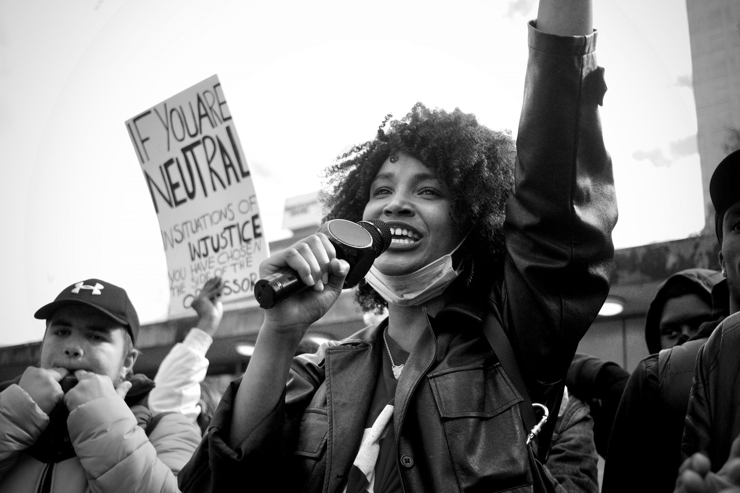 Woman holding a mic and raising her fist at a Black Lives Matter protect