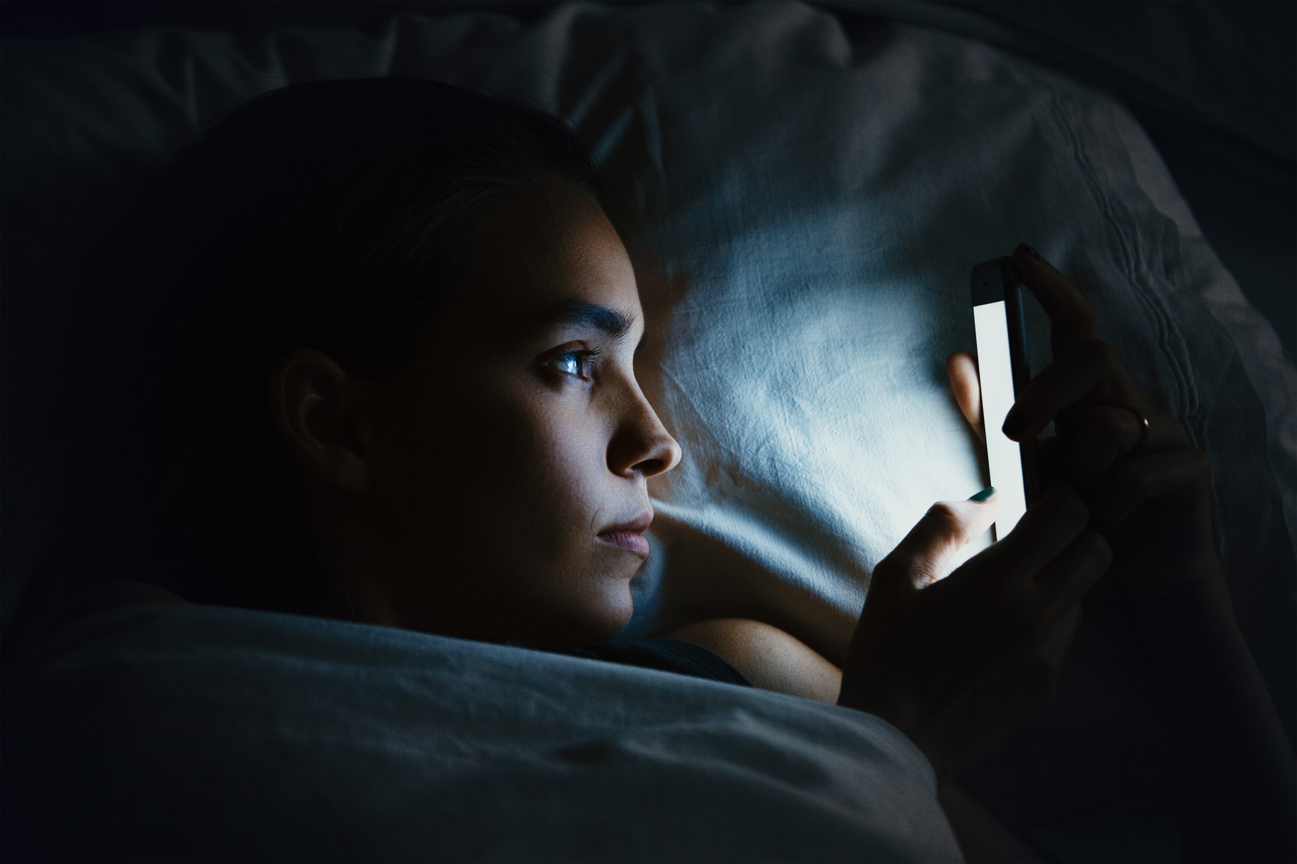 A Woman In Bed Looking At Her Phone