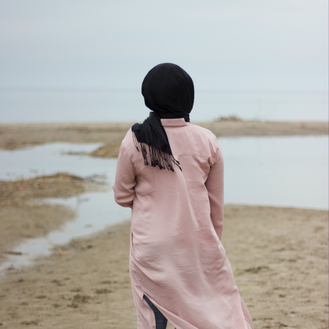 Woman in hijab looking out at a beach