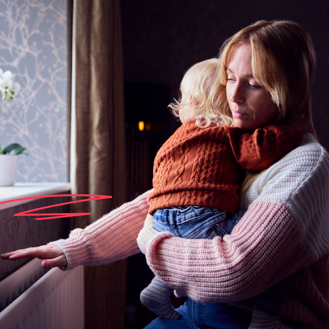 Woman holding her child and feeling above a radiator for warmth