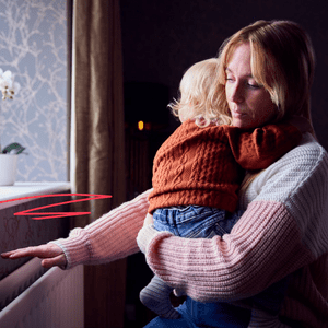 A mother holding her child, feeling above the radiator for warmth